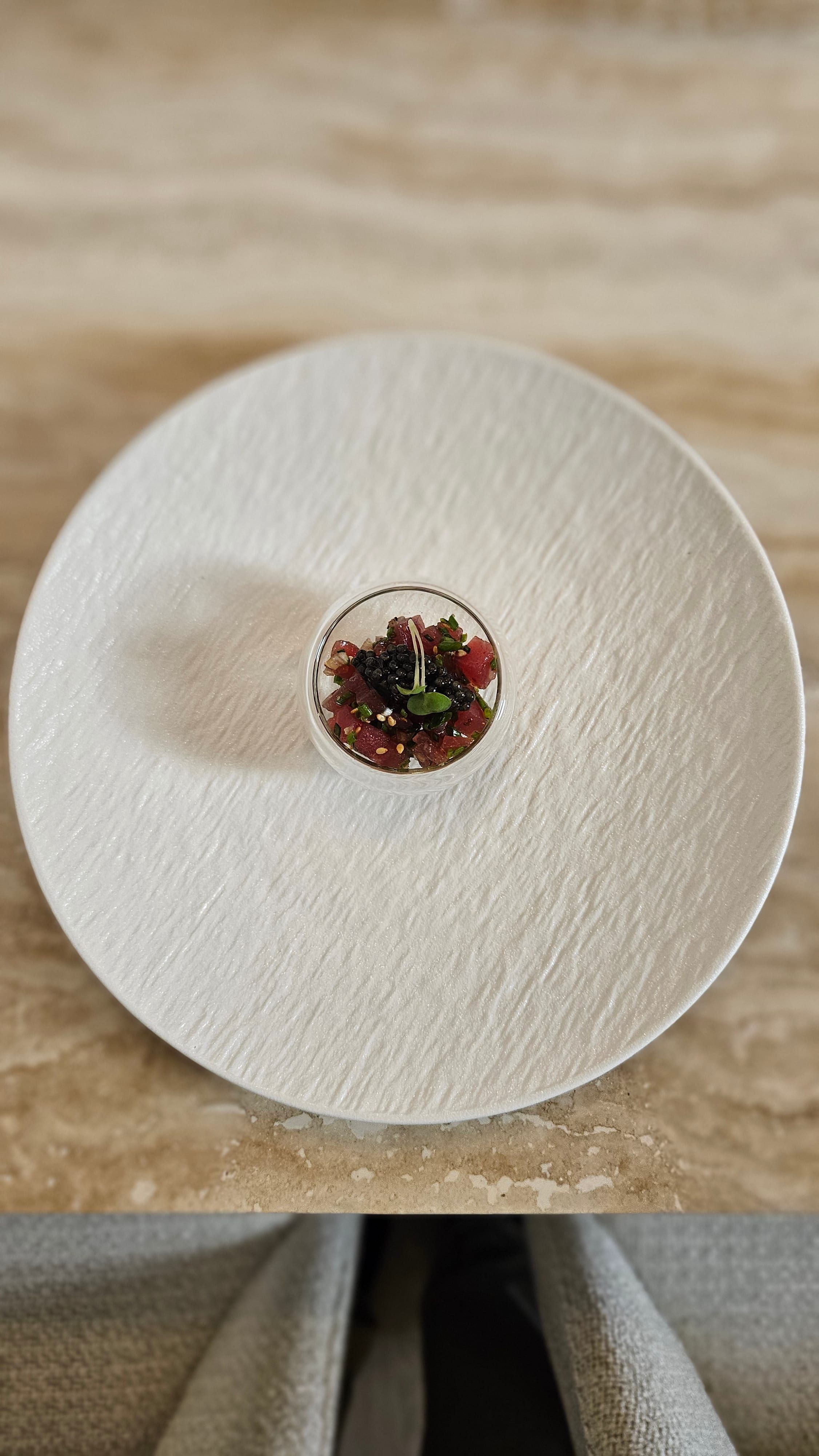 A caviar-topped tartare served in a glass, on a white plate.