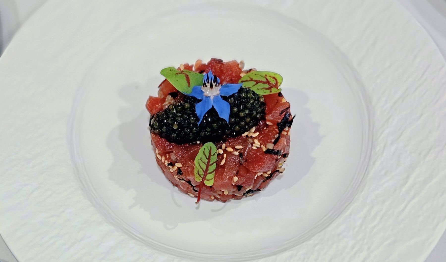 Tartare de thon rouge, caviar, fleur de bourrache et feuilles d’oseille sanguine, sur assiette blanche.