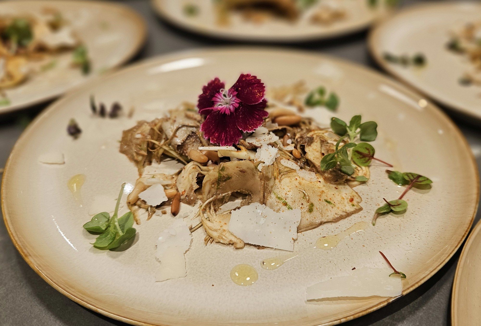 Artichokes with shaved parmesan, pine nuts and an edible flower, plated on stoneware.