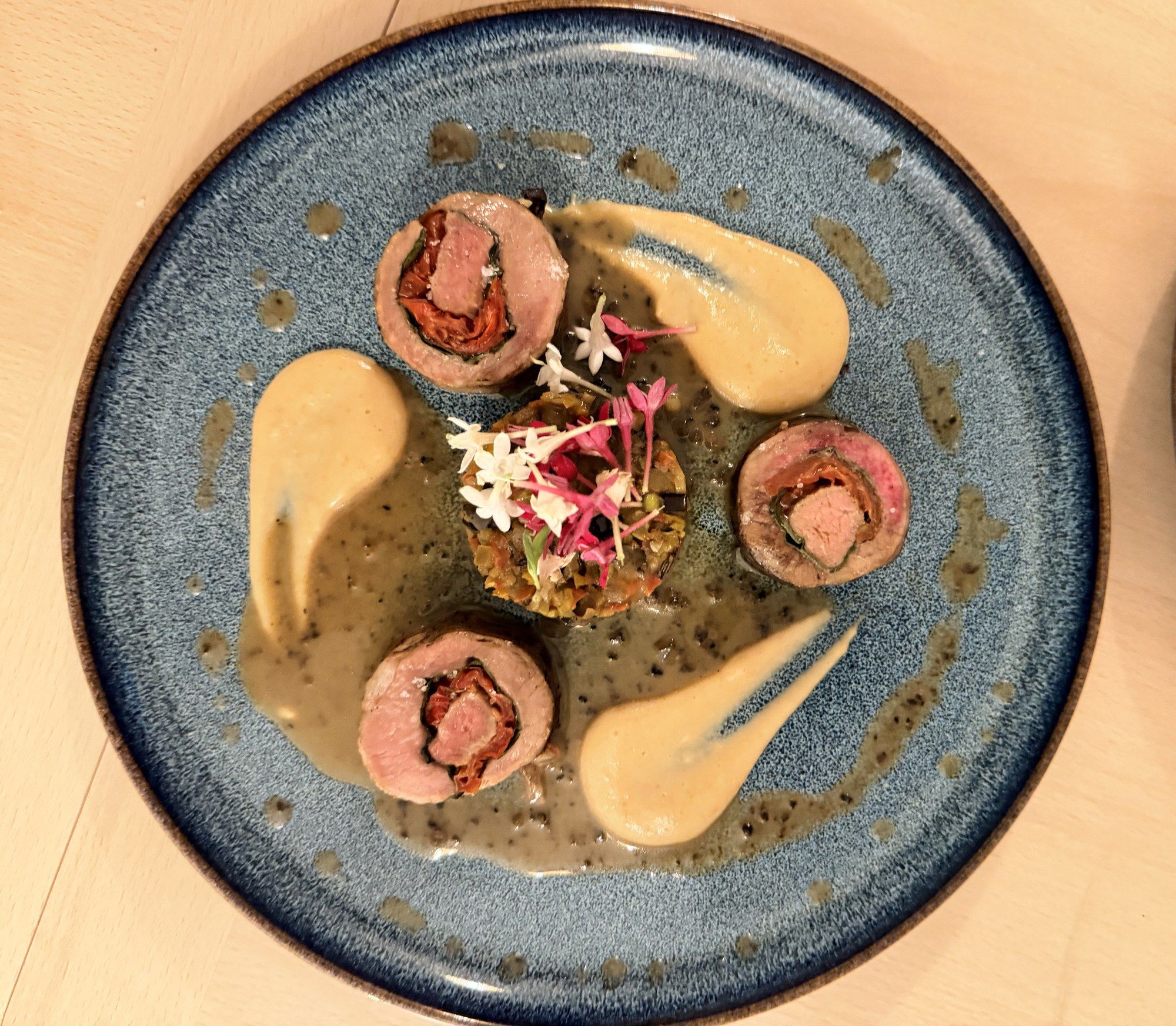 Rolled fillet in three medallions, two sauces and a herb condiment, on a blue glazed plate.
