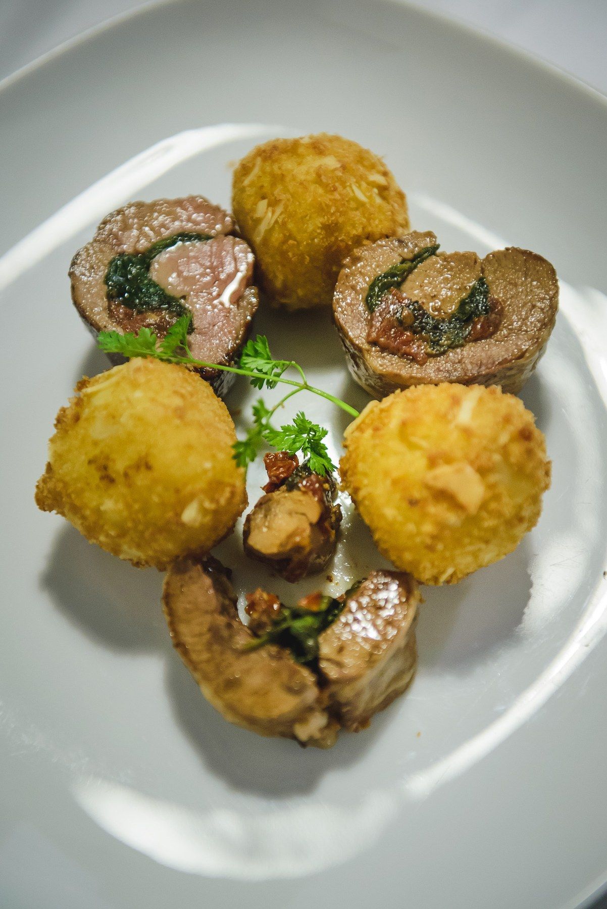Golden crumbed croquettes and slices of a stuffed roulade, plated on white porcelain.